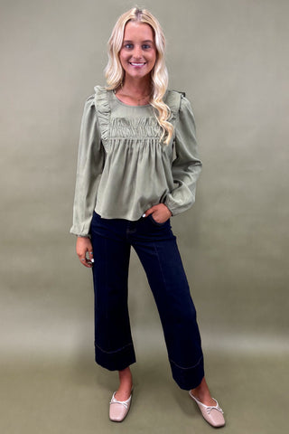 Woman wearing a green blouse and dark jeans against a plain background