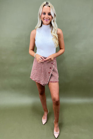 Woman wearing a white top and plaid skirt against a green background