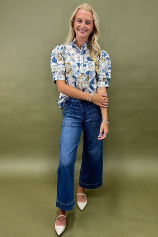 Woman wearing a floral blouse and blue jeans against a green background