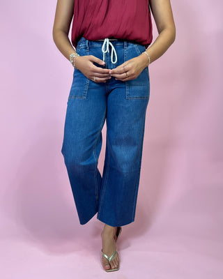 Person wearing blue jeans and a red top on a pink background