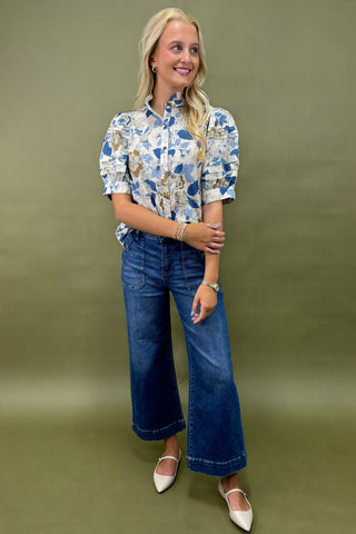 Woman wearing a floral blouse and blue jeans against a green background
