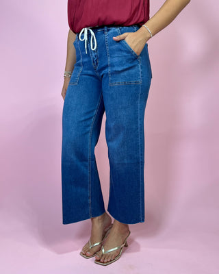 Person wearing blue jeans and a red top on a pink background