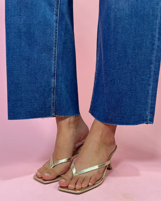 Gold high-heeled sandals worn with blue jeans on a pink background