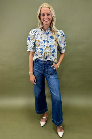 Woman wearing a floral blouse and blue jeans against a green background