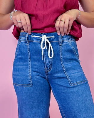 Person wearing a red top and blue jeans with a pink background