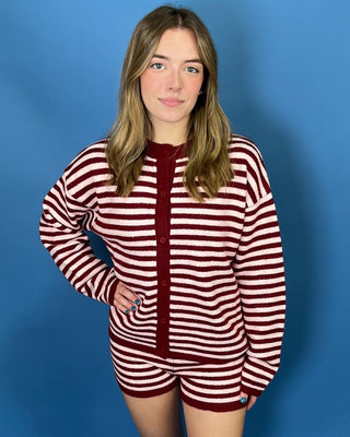 A young woman modeling a matching knit two-piece loungewear set consisting of a long-sleeve button-up cardigan and shorts, featuring horizontal burgundy and off-white stripes