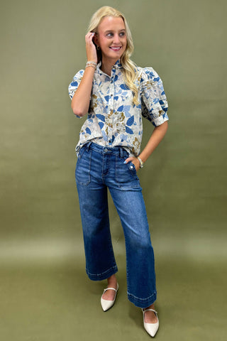 Woman wearing a floral blouse and blue jeans against a green background