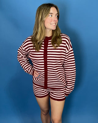 A woman modeling a matching two-piece knit loungewear set consisting of a long-sleeve cardigan and shorts, featuring horizontal burgundy and off-white stripes with a solid burgundy front 