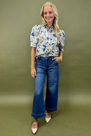 Woman wearing a floral blouse and blue jeans against a green background