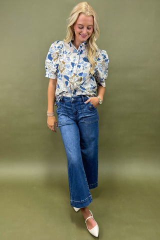 Woman wearing a floral blouse and blue jeans against an olive green background