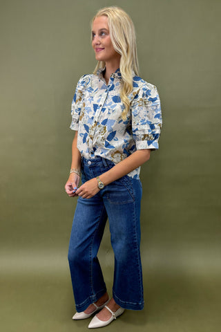 Woman wearing a floral blouse and blue jeans against a green background