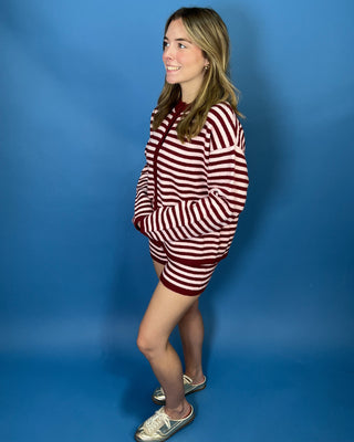 A woman modeling a red and white horizontally striped knit sweater dress with a mock neck and front pockets