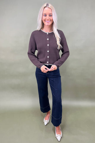 Woman wearing a brown cardigan and dark blue jeans against a green background