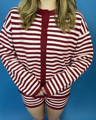 A person wearing a red and off-white striped knit cardigan with matching striped shorts,