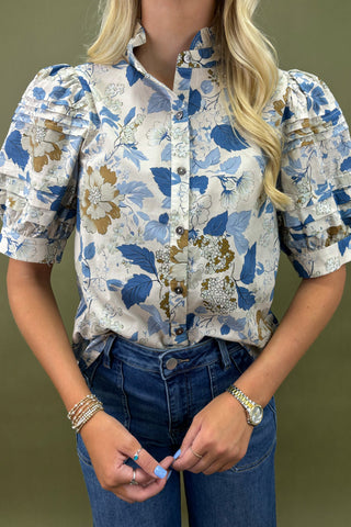 Person wearing a floral blouse with short sleeves and blue jeans on a green background