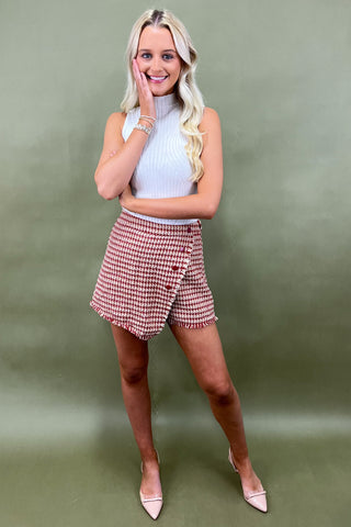 Woman wearing a white top and red checkered skirt against a green background