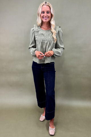 Woman wearing a green blouse and dark jeans against a plain background