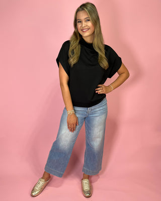 Woman wearing a black turtleneck and blue jeans against a pink background