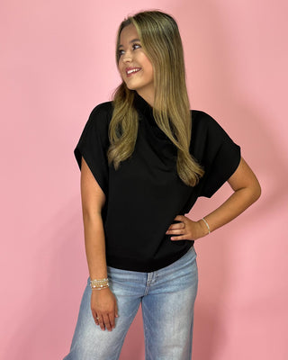 Woman wearing a black top and blue jeans against a pink background