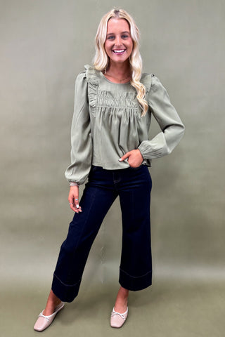 Woman wearing a green blouse and dark blue jeans against a plain background