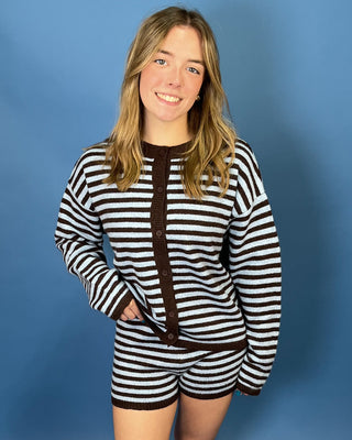 wearing a matching knit two-piece set consisting of a long-sleeve cardigan and shorts. The set features horizontal black and white stripes with solid dark brown trim and a brown button placket.