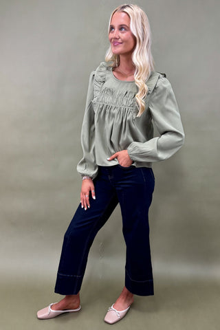 Woman wearing a green blouse and dark blue jeans against a plain background