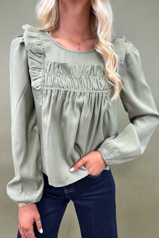 Woman wearing a light green blouse with ruffled shoulders against a neutral background