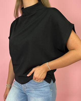 Person wearing a black top and blue jeans against a pink background