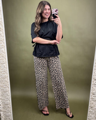 Woman taking a mirror selfie wearing a black top and leopard print pants on a green background