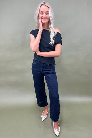 Woman wearing a black top and blue jeans against a plain background