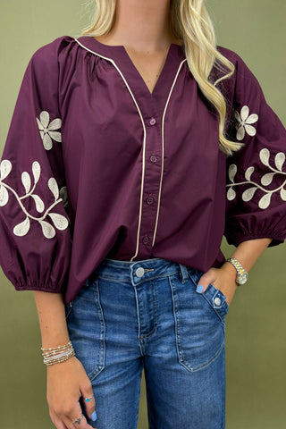 Purple blouse with floral embroidery and blue jeans on a green background