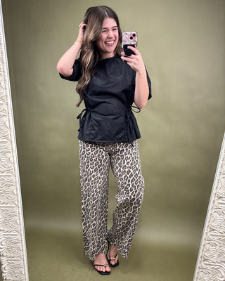 Woman taking a mirror selfie wearing a black top and leopard print pants on a green background
