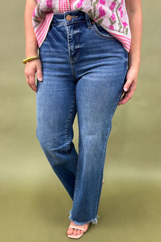 Person wearing blue jeans and a patterned top on a green background