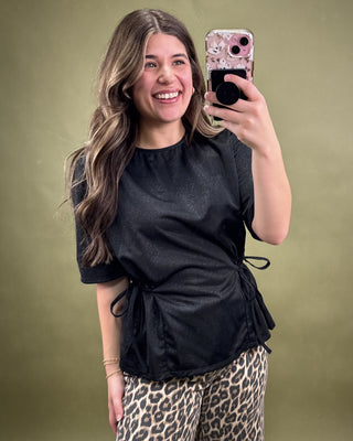 Woman taking a selfie wearing a black top and leopard print pants on a green background