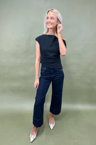Woman wearing a black top and blue jeans against a green background
