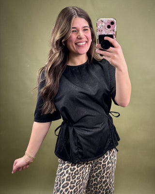 Woman taking a selfie wearing a black top and leopard print pants against a green background