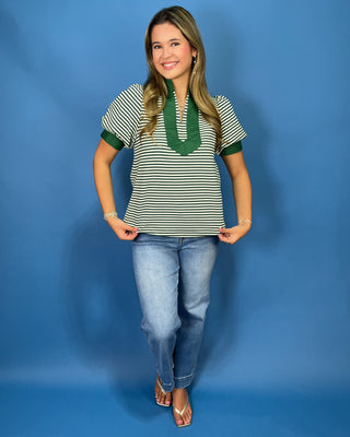 A woman modeling a short-sleeve knit top with green and white horizontal stripes, featuring a solid green V-neckline and sleeve cuffs