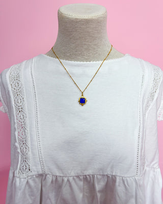 White lace-trimmed top with a gold necklace on a mannequin against a pink background