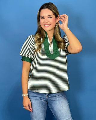 A woman modeling a short-sleeve knit top with green and white horizontal stripes, featuring a solid green V-neckline and sleeve cuffs