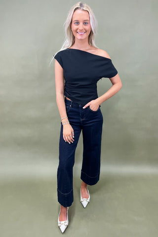 Woman wearing a black off-shoulder top and blue jeans against a plain background