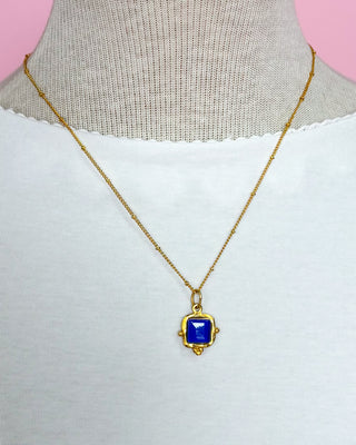 Gold necklace with a blue pendant on a mannequin against a pink background