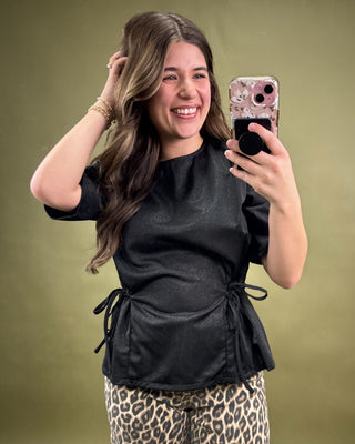 Woman taking a selfie wearing a black top and leopard print pants on a green background