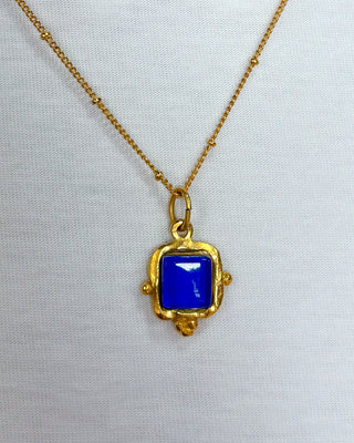 Gold necklace with a blue pendant on a white background