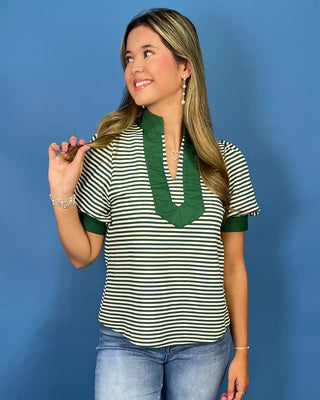 A woman modeling a short-sleeve top with green and black horizontal stripes, featuring a solid green split neckline and green sleeve cuff