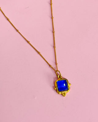 Gold necklace with a blue pendant on a pink background