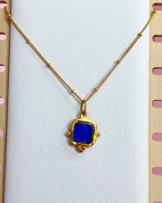 Gold necklace with a blue pendant on a white background