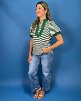 A woman modeling a short-sleeve striped top with green trim and blue jeans