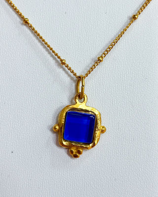 Gold necklace with a blue pendant on a white background