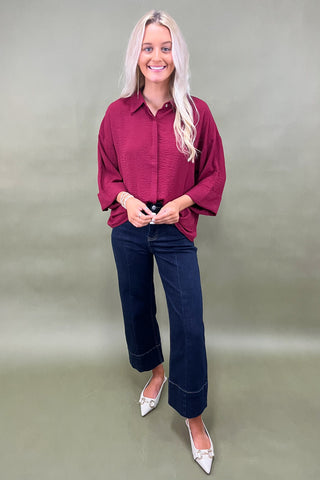 Woman wearing a burgundy shirt and blue jeans against a plain background