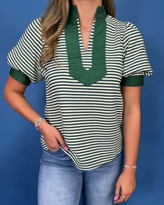 A woman wearing a green and white striped short-sleeve top with a dark green ruffled split neckline, paired with light blue jeans